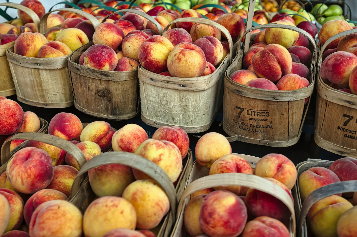 Fresh Canadian peaches in wooden baskets at farmers market, showing vitamin-rich fruit for peach persimmon smoothie research